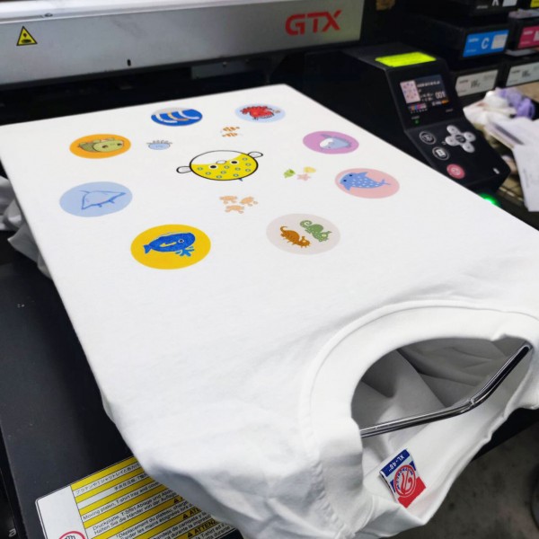 เครื่องพิมพ์ DTG กำลังพิมพ์ลายหลายสีลงบนเสื้อยืดสีขาว จากภาพกระบวนการผลิตของบริษัท ลมหายใจ จำกัด